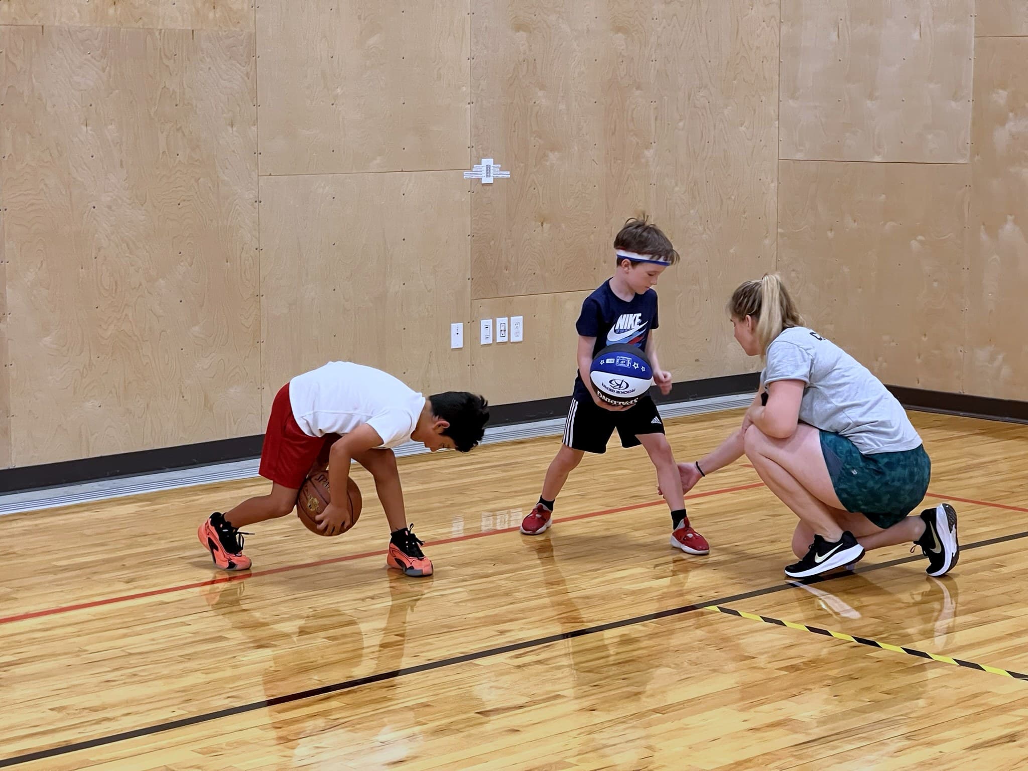 A Wildcats coach guiding two young players through a low dribbling stance